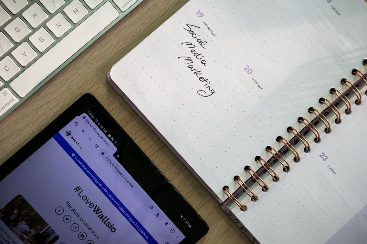 hero-img Top view of a notebook, tablet, and keyboard used for social media marketing planning.
